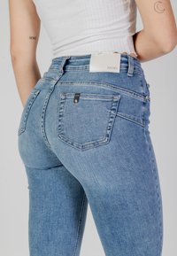Jeans skinny in denim blu con un lavaggio chiaro, dotati di un'etichetta bianca del marchio sul retro e di un piccolo dettaglio della tasca nera.