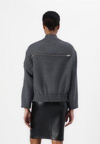Graue Wollbomberjacke mit einem Reißverschlusstasche an der Rückseite, elastischem Bund und lockeren Ärmeln, kombiniert mit einem schwarzen Lederbleistiftrock.