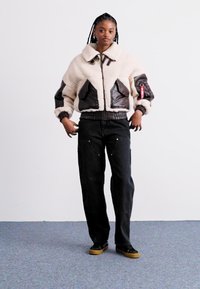Giacca in finta pelliccia color crema con dettagli in pelle marrone, chiusura con zip e polsini a costine. Abbinata a pantaloni oversize neri e sneakers.