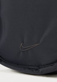 Borsa Nike in tessuto blu scuro texturizzato, forma arrotondata e logo grigio ricamato discreto. Le cuciture sono visibili lungo i bordi.