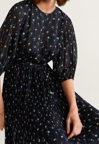Robe plissée bleu marine avec imprimé floral, décolleté rond et manches ballon. Le tissu a une texture transparente avec un détail de taille cintrée.