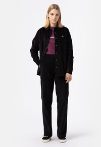 Conjunto de camisa de pana negra y pantalones con una camiseta burdeos. Presenta botones en la camisa y zapatos negros sólidos con suelas blancas.