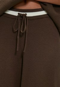 Bruine gebreide sweatpants met een witte gestreepte tailleband, met een trekkoord en een zachte, gestructureerde stof.