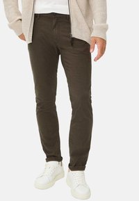 Donkergroene katoenbroek met een slim fit en een gestructureerde oppervlakte, gecombineerd met witte sneakers. Zichtbare rits- en knoopsluiting.