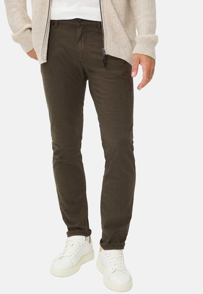 Donkergroene katoenbroek met een slim fit en een gestructureerde oppervlakte, gecombineerd met witte sneakers. Zichtbare rits- en knoopsluiting.