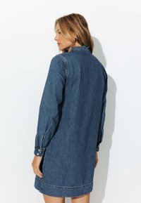 Robe en denim bleu foncé avec des manches longues, un col volé, des poignets boutonnés et une coupe droite. Elle présente une ourlet au-dessus du genou.