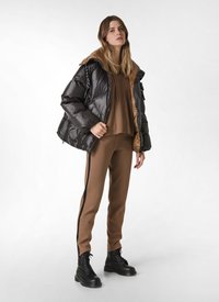 Zwarte pufferjack met bruine accenten, gecombineerd met een bruine hoodie en bijpassende кепaalkjes met zijkanten in zwart. Zwarte veterlaarzen.