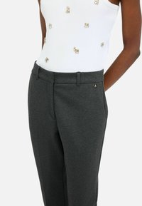 I pantaloni grigi su misura presentano una texture liscia con una parte anteriore piatta, tasche laterali e un piccolo logo sulla vita.