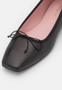 Ballet flat en cuir noir avec un bout carré, featuring un détail de nœud fin. L'intérieur est rose pâle avec une texture lisse.