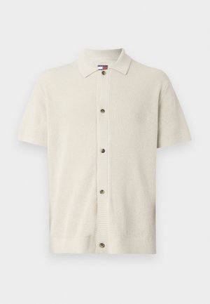 Kréma krāsas īsām piedurknēm kardigāns, izgatavots no teksturēta adījuma auduma, ar apkakles dekoltē un piecām brūnām pogām priekšpusē.