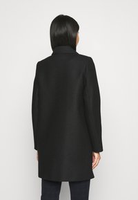 Abrigo de lana negro con un cuello clásico, mangas largas y líneas simples. Presenta un acabado texturizado y un corte a media longitud.