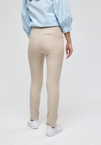 Bežové kostkované kalhoty s úzkým střihem, které mají texturovanou látku, kapsy na pase a hladký povrch, doplněné o bílé tenisky.