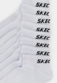 White cotton crew socks with ribbed cuffs, featuring black "SKECHER" text logo on the ankle, neatly stacked in a row.
