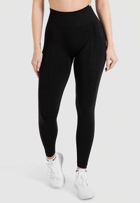 Svarta högmidjade leggings i stretchigt material med en slät yta och subtila sömmar. Bärs med vita sportskor.