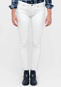 Jeans ajustados blancos con cinco bolsillos, cierre de botón y ligera elasticidad, combinados con botas negras hasta el tobillo con paneles laterales elásticos.