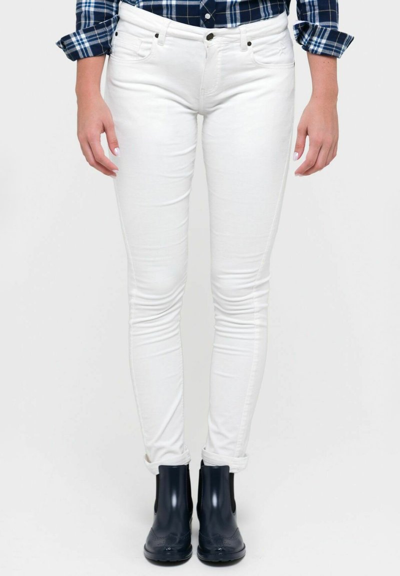 Jeans ajustados blancos con cinco bolsillos, cierre de botón y ligera elasticidad, combinados con botas negras hasta el tobillo con paneles laterales elásticos.