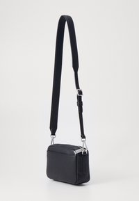 Musta nahkainen olkalaukku jossa on teksturoitu pinta, suorakulmainen muoto, säädettävä hihna ja hopeanväriset metalliosat.