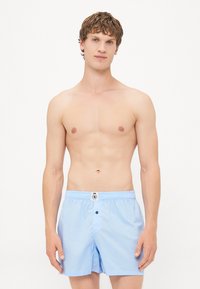 Helleblaue Badeshorts aus leichtem Material, mit einem elastischen Bund, einem Knopfverschluss und einem Logodetail auf der Vorderseite.