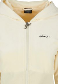 Hoodie zippé crème clair avec une fermeture éclair en métal et un logo brodé sur la poitrine. Tissu doux avec une texture lisse. Taille petite.
