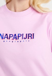Jasnoróżowy sweter z dużym, wielokolorowym logo "NAPAPIJRI" w nowoczesnej czcionce oraz napisem "geographic" w mniejszym rozmiarze poniżej.