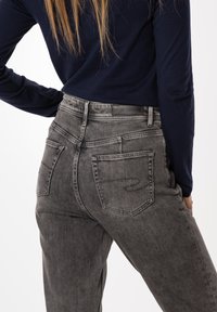 Szare dżinsy z wysokim stanem o wyblakłej fakturze, z dwoma tylnymi kieszeniami i przeszyciami dekoracyjnymi. Noszone z granatową bluzką z długim rękawem.