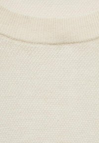 Țesătură tricotată de culoare crem, cu o textură fină. Decolteu rotund ribat cu variații subtile în țesătură pe întreaga suprafață a materialului.