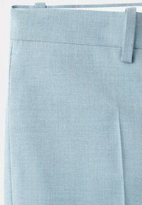 Lysblåt buksestof nærbillede, der viser linning, bæltestropper og frontplissédetalje.