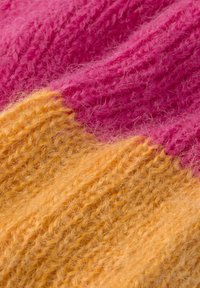 Nærbillede af fuzzy strikstof med ribbet tekstur, der har livlige farveblokke i pink og orange.