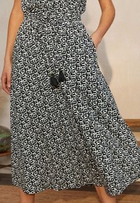 Jupe maxi à motif noir et blanc avec une taille élastique et un cordon de serrage. Comprend deux poches latérales et des accents de franges.