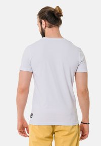 Weißes T-Shirt mit kurzen Ärmeln, rundem Ausschnitt und kleinem schwarzen Markenlogo unten links. Glattes Material, taillierte Passform.