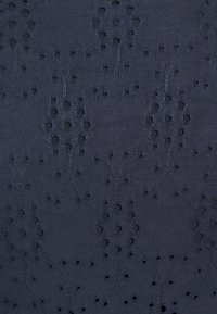 Marinblå textil med ett mönster som har utskurna hål i en diamant- och cirkelmotiv. Texturen är slät och något strukturerad.