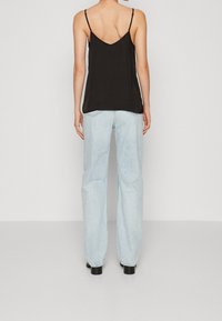 Camicetta nera senza maniche con spalline sottili; abbinata a jeans larghi blu chiaro. Texture liscia, vestibilità casual e design minimalista.
