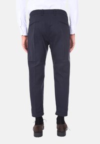 Pantaloni navy con vestibilità affusolata, realizzati in tessuto liscio, con due tasche posteriori e polsini arrotolati. Abbinati a scarpe marroni.