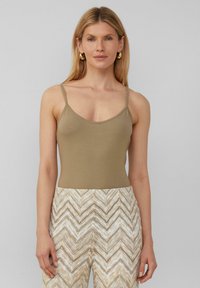 Débardeur ajusté beige avec de fines bretelles, conçu en tissu doux. Associé à un pantalon taille haute à motif zigzag crème et beige.