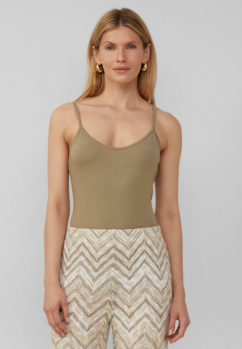 Débardeur ajusté beige avec de fines bretelles, conçu en tissu doux. Associé à un pantalon taille haute à motif zigzag crème et beige.