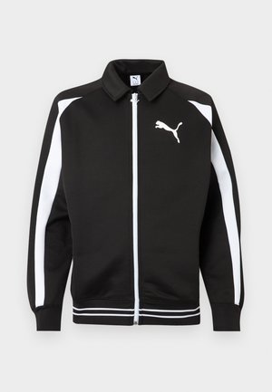 Juoda sportinė striukė su užtrauktuku, baltos juostelės ant rankovių, baltas Puma logotipas ant krūtinės ir baltos juostelės apačioje.