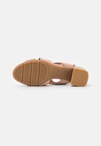 Sandale à talon épais, semelle en caoutchouc avec adhérence texturée et trous de ventilation, empeigne en daim de ton rose beige clair.
