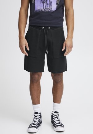 Șorturi negre texturate cu două buzunare frontale, talie ajustabilă cu șnur, asociate cu un tricou grafic bleumarin și adidași înalți.