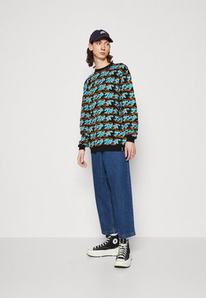 Black sweatshirt with colorful abstract pattern, denim wide-leg pants, and black high-top sneakers. Cap completes the look.
