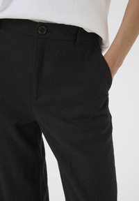 Pantaloni di lino neri con una texture liscia, dotati di chiusura con bottone e tasche laterali, progettati con un taglio dritto.