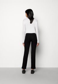 Vaqueros negros acampanados con una cintura de altura media y dos bolsillos traseros, combinados con una blusa blanca de manga larga con relieve y zapatos negros.