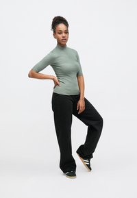 Πράσινο ριμπ κοντομάνικο τοπ σε συνδυασμό με μαύρο παντελόνι φαρδιάς γραμμής και σκούρα αθλητικά παπούτσια. Το τοπ διαθέτει ψηλό λαιμό και υφή στο ύφασμα.