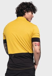 Żółta i czarna koszulka polo z krótkim rękawem charakteryzuje się teksturowanym wzorem, zaokrąglonym dołem oraz zasuwaną kieszenią na plecach do przechowywania.