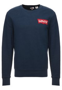 Námořnická modrá mikina vyrobená z bavlny, s červenou nášivkou na hrudi, žebrovanými manžetami a kulatým výstřihem.