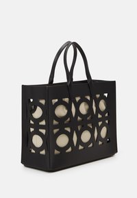 Sac fourre-tout noir perforé avec des découpes circulaires, doté de poignées noires lisses et d'une doublure intérieure beige. Forme rectangulaire structurée.