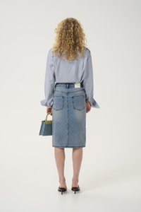 Μπλε τζιν φούστα με εφαρμοστή σχεδίαση, μήκους μέχρι το γόνατο. Ανοιχτό μπλε πουκάμισο με μακριά μανίκια και μικρή πράσινη και μπλε τσάντα. Απλά μαύρα τακούνια.