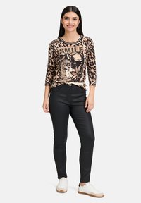 T-shirt à manches longues avec imprimé léopard et graphique "SMILE", associé à un pantalon noir ajusté et des baskets blanches avec des accents beige. Texture de tissu lisse.