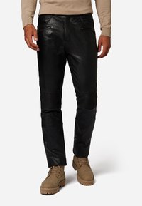 Zwarte leren broek met een slim fit, geribbelde knieaccenten en voorzakken met rits. Gepaard met tan kleurige veterschoenen voor contrast.