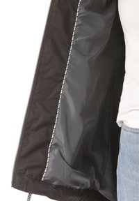 Svart jacka med reflekterande silverfoder som hålls öppen av en person i vit skjorta och ljusblå jeans.