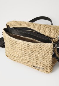 Borsa a tracolla in paglia intrecciata con tasca a zip nera, superficie testurizzata e logo stampato. Presenta una tracolla robusta e foderatura interna.